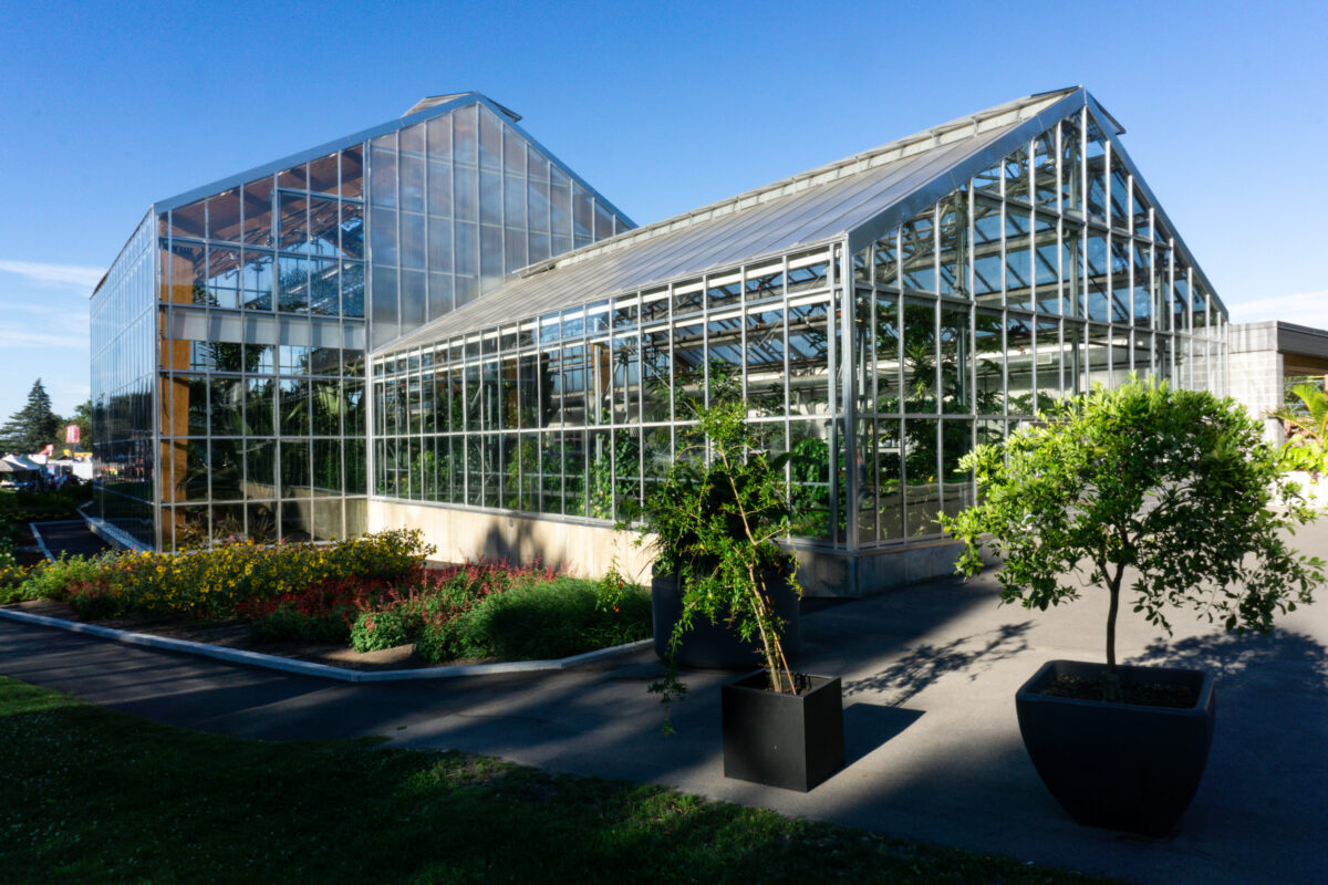Glass-fronted Gage Park Tropical Greenhouse with trees and garden beds outside.